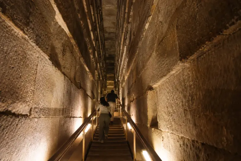 Visitor climbing the lit ascending passage inside the Great Pyramid